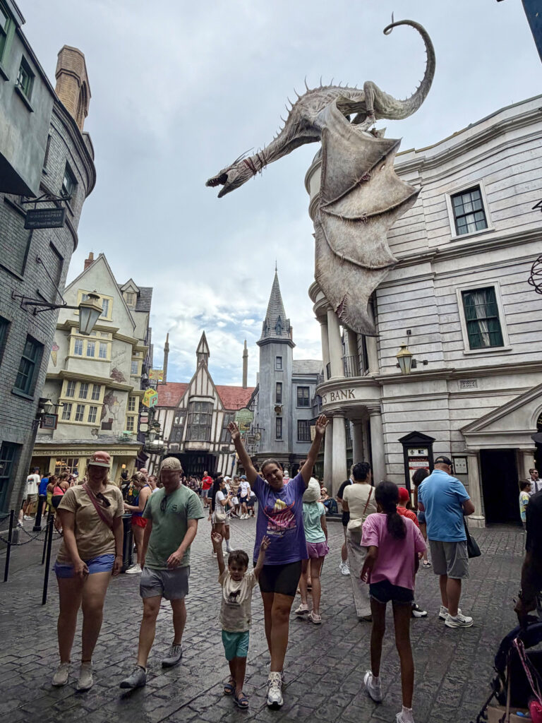Grupo de visitantes no Beco Diagonal com o dragão do Gringotes ao fundo, no Universal Studios Florida