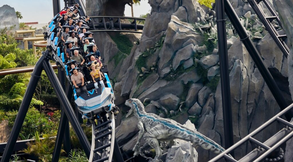 Visitantes na montanha-russa Jurassic World VelociCoaster, com um velociraptor ao lado do trilho, no Islands of Adventure